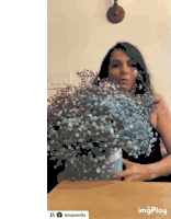 a woman is sitting at a table with a vase filled with baby 's breath .