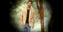 a man in a tan jacket and black shirt is standing in a forest