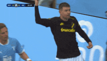 a soccer player wearing a truecalle jersey holds up his arm