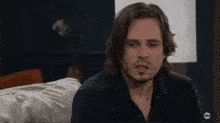 a man in a black shirt is sitting on a couch with abc written on the bottom