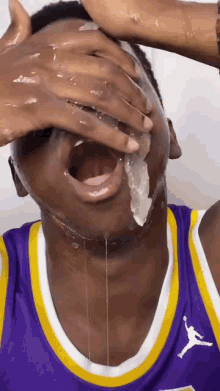 a man in a purple and yellow jordan jersey is covering his face