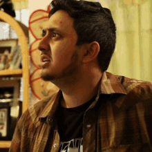 a man wearing a plaid shirt and a black t-shirt with the word fat on it looks to the side