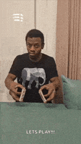 a man in a black shirt with an elephant on it is holding two playing cards in his hands .