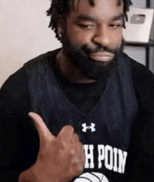 a man with a beard is wearing a black under armour jersey and giving a thumbs up .