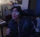 a man wearing glasses and a leather jacket is sitting at a keyboard