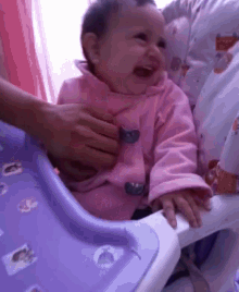 a baby in a pink coat is sitting in a high chair and crying