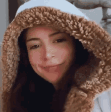 a woman wearing a furry hooded jacket is smiling .