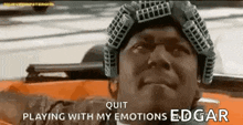 a man wearing a helmet is sitting in a car with the words `` quit playing with my emotions edgar '' .