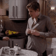 a man in a grey shirt is standing in a kitchen adjusting his shirt