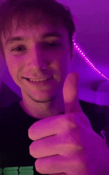 a young man is giving a thumbs up sign in front of a purple light .