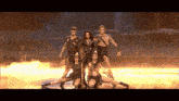 a group of dancers are posing for a picture on a stage with flames behind them