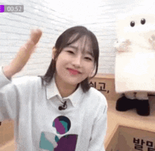 a woman in a white sweater is sitting in front of a box with a stuffed animal behind her .
