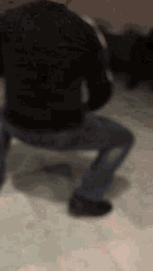 a man in a black shirt and blue jeans is squatting down on the floor .