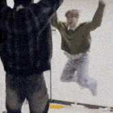 a man in a green sweater is jumping in the air while another man watches .