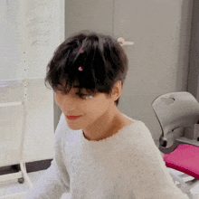 a young man in a white sweater is sitting in a chair with a pink pillow .