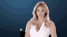 a woman in a white dress is sitting in a chair and looking at the camera .