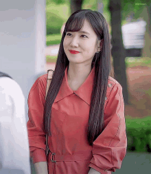 a woman wearing a red trench coat and red lipstick smiles for the camera