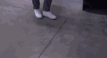 a person wearing white sneakers and gray pants is standing on a concrete floor .