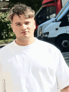a young man in a white shirt stands in front of a row of vans