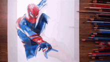 a drawing of a spiderman is on a wooden table with colored pencils