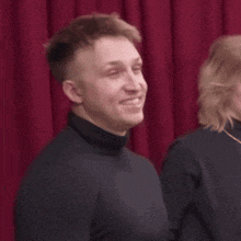 a man in a black turtleneck stands next to a woman in a black sweater