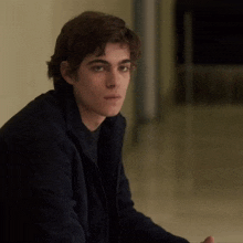 a young man in a black jacket is sitting on the floor looking at the camera