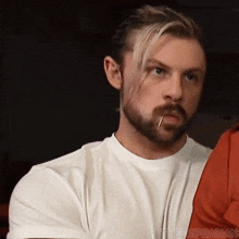 a man with a beard and blonde hair is wearing a white t-shirt and smoking a cigarette .