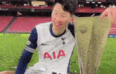 a soccer player wearing a white aia jersey holds a trophy