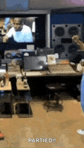 a man is standing in front of a television in a room with a desk and a stool .