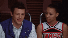 a woman in a wmhs cheerleader uniform sits next to a man in a blue vest