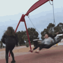 two girls are playing on a red swing set