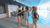 a group of women in swimsuits are standing near a pool
