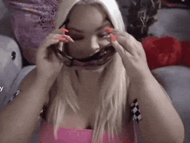 a woman in a pink top is covering her face with a scarf and sunglasses .