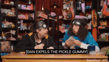 two men are sitting at a table and one of them is saying dan expels the pickle gummy
