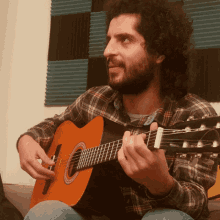 a man in a plaid shirt plays an acoustic guitar