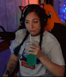 a woman wearing headphones and a senpai shirt drinks a blue drink