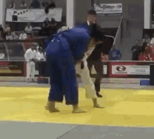 a judo match is being played on a yellow mat in a stadium .