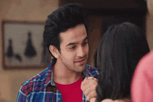 a woman wearing a yellow top and a necklace smiles at a man in a plaid shirt