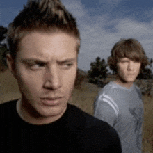 a man in a black shirt stands next to another man in a grey shirt in a field