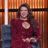 a woman in a red dress is sitting in a chair with her hands folded and smiling .