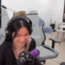 a woman wearing headphones is smiling while holding a purple microphone .