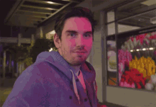 a man in a hoodie with a smiley face on it stands in front of a window