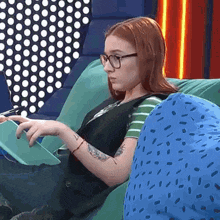 a woman with red hair and glasses is sitting on a couch holding a tablet .
