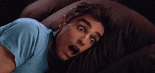 a man in a blue shirt is laying on a couch with his mouth open and his eyes closed .