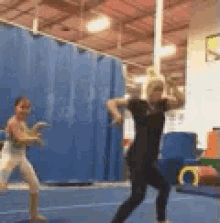 a woman is standing on a balance beam in a gym while a boy looks on .