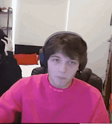 a young man wearing headphones and a pink shirt is sitting in a chair .