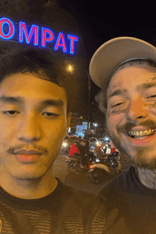 two men are posing for a picture in front of a ompat sign