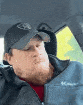 a man with a beard is sitting in a car wearing a hat and a columbia jacket .