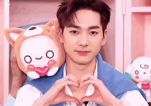 a young man is making a heart shape with his hands while holding a stuffed animal