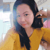 a woman in a yellow shirt is taking a selfie with her hand in her hair